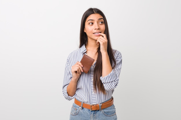 La mujer árabe joven que sostenía una cartera se relajó pensando en algo que miraba un espacio en blanco.