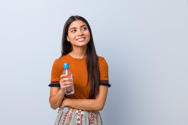 Mujer árabe joven que sostiene una botella de agua que sonríe confiada con los brazos cruzados.