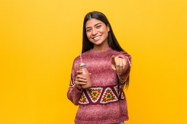 Mujer árabe joven que sostiene un smoothie sonrisas alegres que señalan al frente.