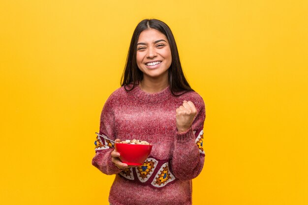 Mujer árabe joven que sostiene un tazón de cereal que anima despreocupado y emocionado. Concepto de victoria