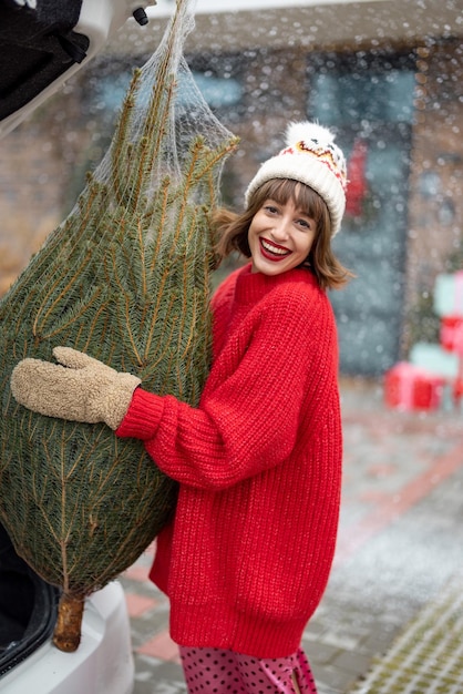 Mujer con árbol de navidad envuelto cerca de la casa preparándose para las vacaciones de invierno