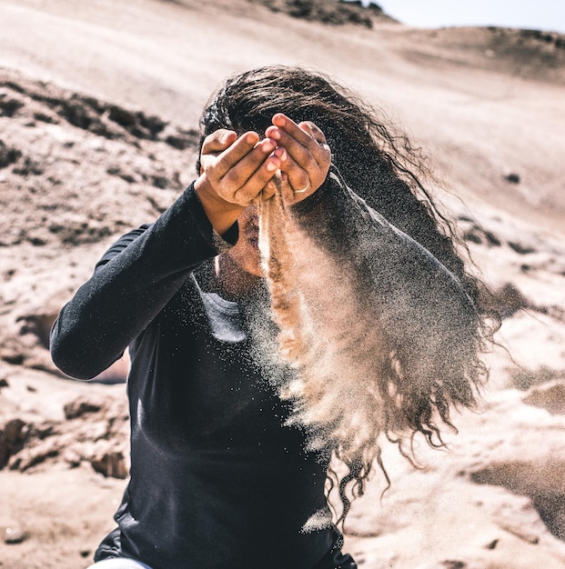 Foto mujer con arena cayendo de las manos en el desierto