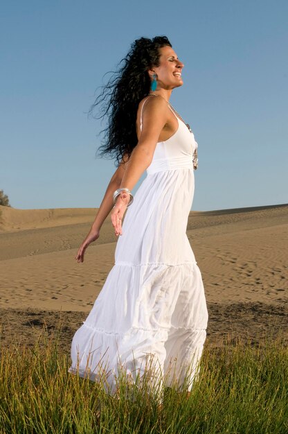 Mujer en la arena disfrutando del sol de primavera o verano vestida con ropa blanca