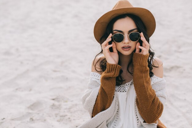 Mujer en la arena tocando gafas de sol