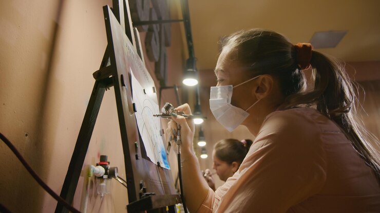 Foto mujer artista aprende a pintar con aerógrafo con papel de tinte acrílico y caballete