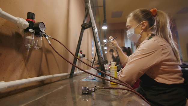 Mujer artista aprende a pintar con aerógrafo con papel de tinte acrílico y caballete