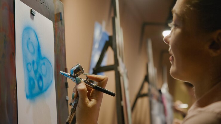 Foto mujer artista aprende a pintar con aerógrafo con papel de tinte acrílico y caballete
