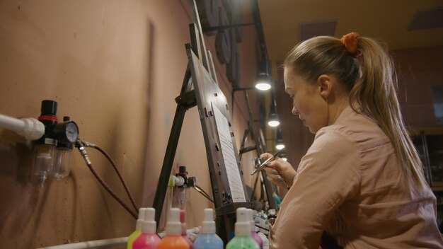 Mujer artista aprende a pintar con aerógrafo con papel de tinte acrílico y caballete