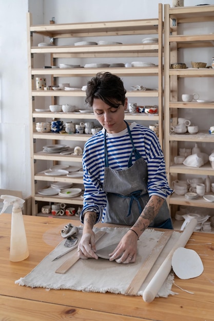 Mujer artista de cerámica de pie en la mesa en el estudio esculpir placa de arcilla cruda