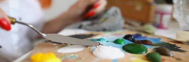 Mujer artista iguala la pintura con una espátula en una paleta de madera manos con pintura de recogida de manicura