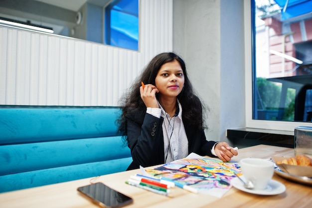 Mujer artista india usa pintura formal y escucha música hindú desde los auriculares mientras está sentada en el café