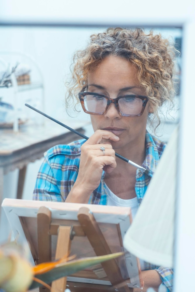 Foto mujer artística pintando en un taller tranquilo y organizado usando herramientas profesionales y colores vibrantes para crear una pieza de arte detallada y expresiva completamente inmersa en su trabajo creativo