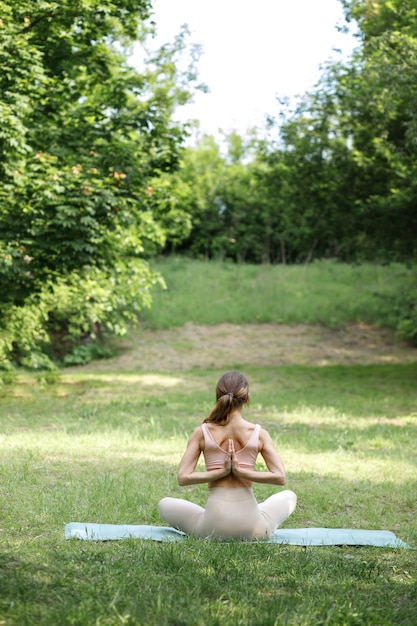 Mujer en asana yoga sobre un fondo verde en el verano. vista trasera