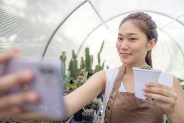 La mujer de Asia disfruta de la jardinería con cactus y es propietaria de una empresa de nueva creación que vende árboles en línea.