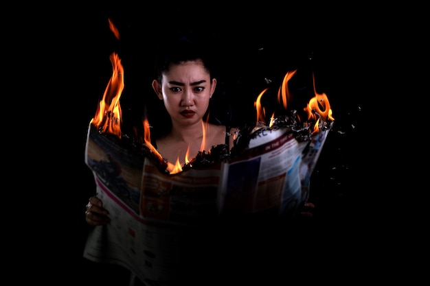 La mujer de Asia está sosteniendo encendida y lee un periódico que quema el fuego en el fondo negro