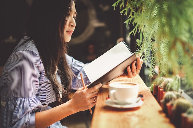Mujer de Asia leyendo un libro y tomando un café en la cafetería