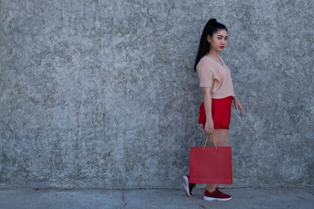 Mujer de Asia sosteniendo bolsas de la compra en el fondo de la pared de hormigón