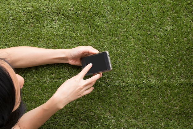 Mujer de Asia usando el teléfono inteligente en la hierba verde