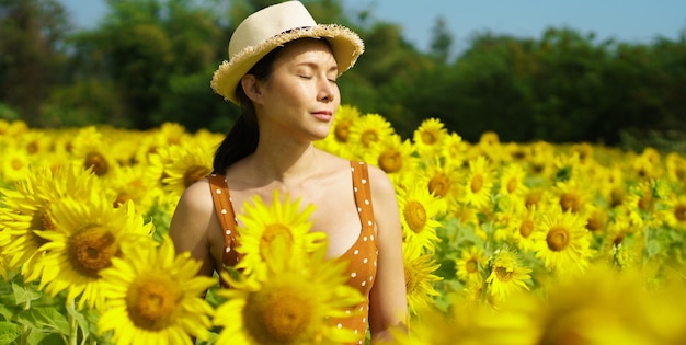 Mujer asiática de 40 años LGBT transgénero expresa el sentimiento Happy Smile divertido bajo el sol en el campo de flores amarillas de Sunflower sobre la montaña del cielo azul Poses femeninas para la fotografía de moda en el paisaje al aire libre