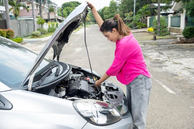 Mujer asiática abriendo el capó del auto y buscando problemas. El auto se descompone