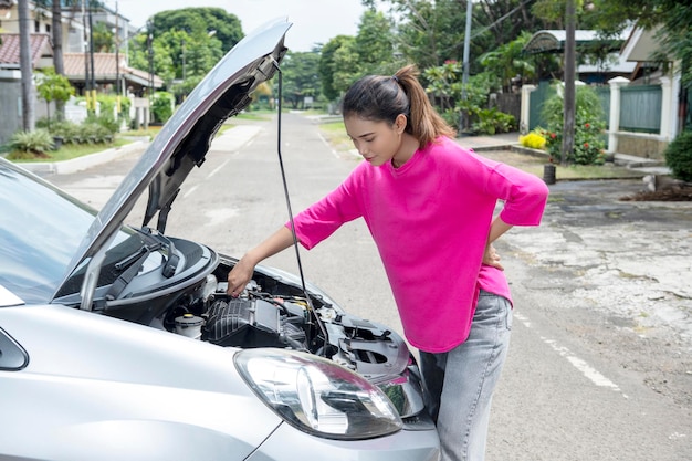 Mujer asiática abriendo el capó del auto y buscando problemas. El auto se descompone
