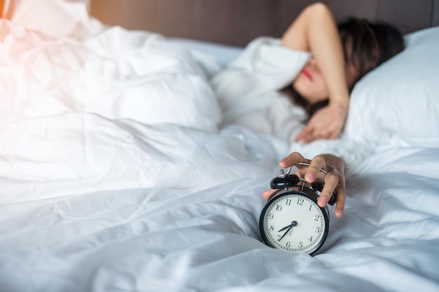 Mujer asiática acostada en la cama por la mañana con despertador retro mujer joven dormir en el dormitorio en casa insomnio inquieto durmiendo conceptos preocupados y estresados