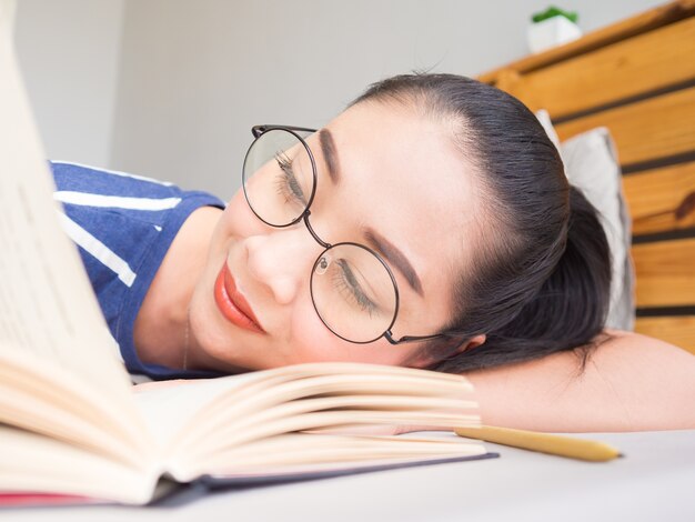 La mujer asiática se acuesta en la cama y el libro de lectura.