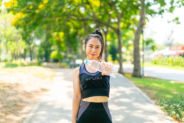 Mujer asiática agua potable en ropa deportiva después del ejercicio en el parque