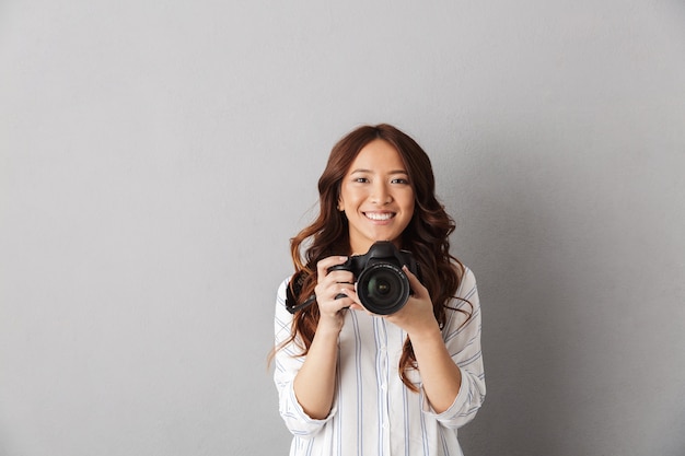 Mujer asiática alegre que se encuentran aisladas, tomando una foto con cámara de fotos