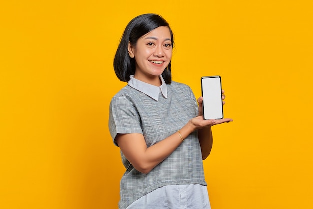 Mujer asiática alegre que muestra la pantalla del smartphone en blanco con la palma. concepto de promoción de productos