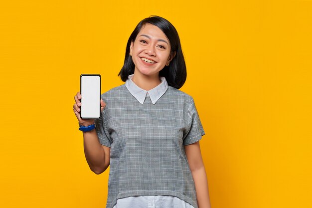 Mujer asiática alegre que muestra la pantalla del smartphone en blanco con la palma. concepto de promoción de productos