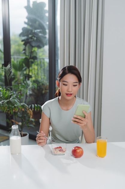 Una mujer asiática almuerza con su teléfono en las manos