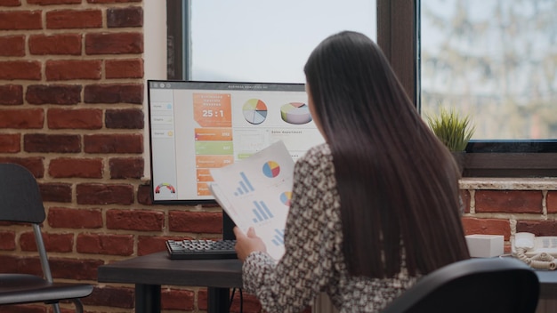 Mujer asiática analizando documentos para planificar un proyecto empresarial en la computadora en la oficina de inicio. Empleado de la empresa que trabaja con documentos para ayudar con el crecimiento y el desarrollo financiero. Trabajador ocupado