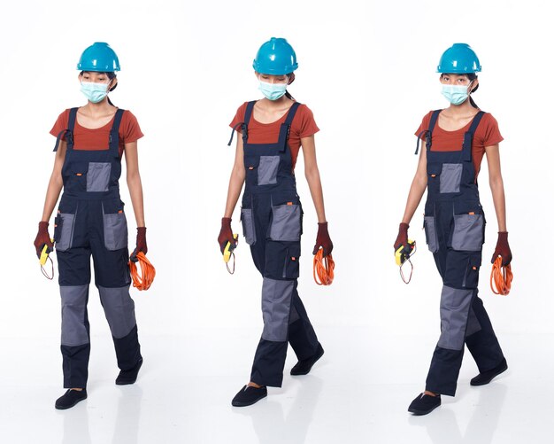 La mujer asiática de los años 20 usa casco y guante de camisa naranja uniforme azul como tipo de reparación de reparación eléctrica con cable. Longitud total del soporte femenino alto sostenga el medidor de voltaje múltiple muchas poses, fondo blanco aislado