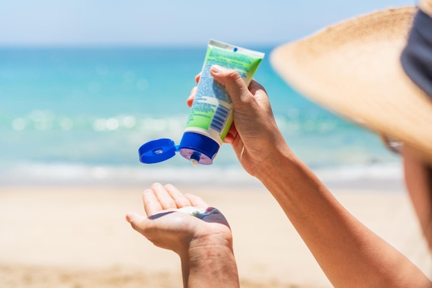 Mujer asiática aplica protector solar en su mano en una playa tropical Chica aplicando bloqueador solar en su piel Protección UV concepto de verano y playa