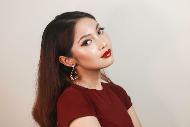 Una mujer asiática de aspecto feroz con un lado de camisa roja posando frente a un fondo blanco