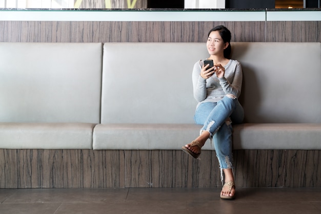 Mujer asiática atractiva joven que sienta la pierna cruzada en el sofá del sofá