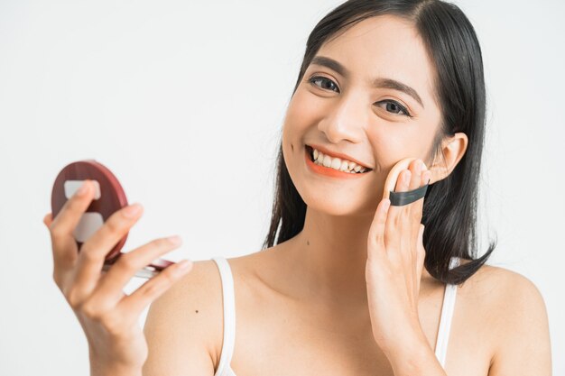 Mujer asiática atractiva que aplica polvos faciales sobre la pared blanca. belleza de asia