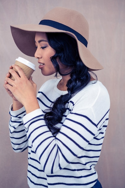 Mujer asiática atractiva con el sombrero que sostiene la taza disponible