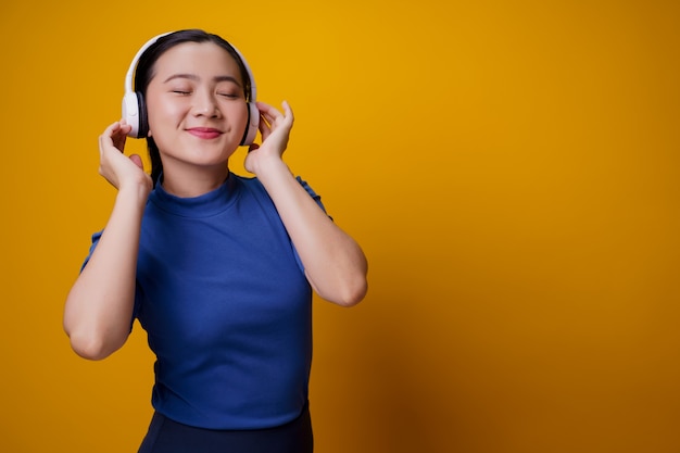 Mujer asiática con auriculares escuchando música bailando en amarillo.