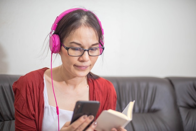 Mujer asiática con auriculares leyendo la Biblia en el teléfono inteligente