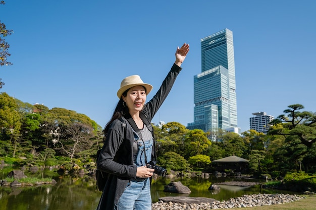 mujer asiática bastante joven presentando el famoso edificio alto con el brazo levantado y sonriendo alegremente.