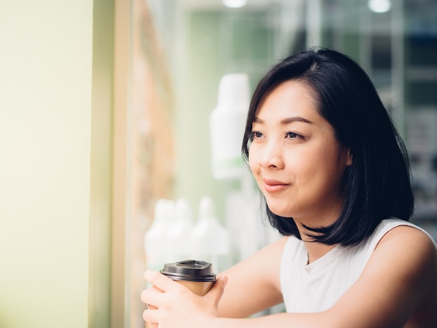 La mujer asiática bebe el café caliente en el café con la luz caliente.