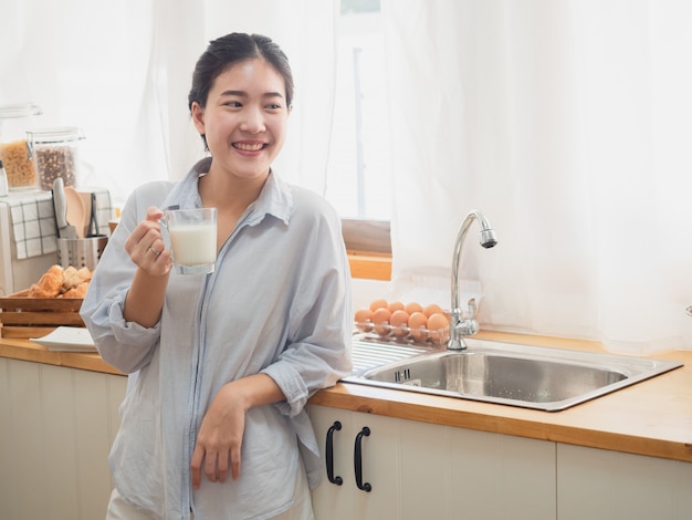 Mujer asiática beber leche en la cocina