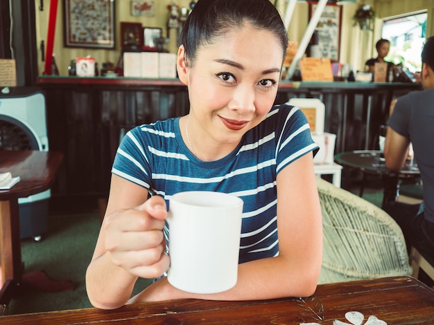 La mujer asiática en bebida y se relaja en café.