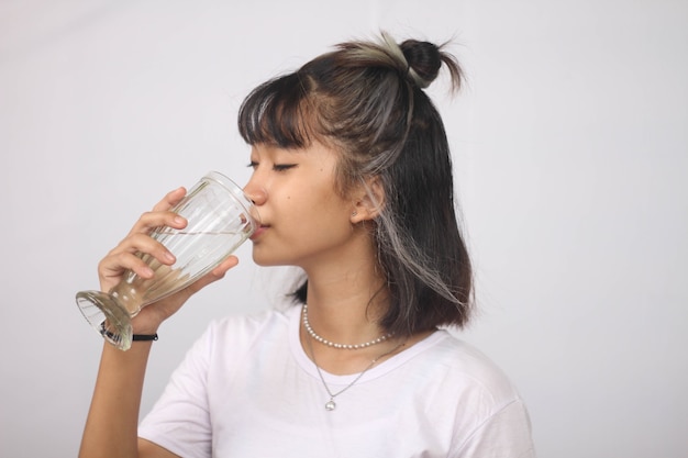 Mujer asiática bebiendo un vaso de agua sobre fondo blanco aislado