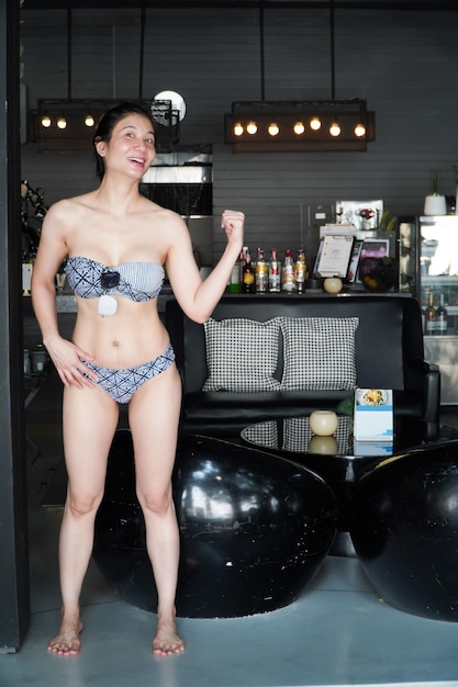 Mujer asiática en bikini está sonriendo brillantemente De pie en un bar decorado en un interior elegante