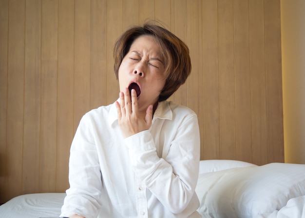 Foto mujer asiática bostezando en la cama.