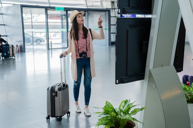 mujer asiática en busca de su vuelo. vuelos que se muestran en el horario.