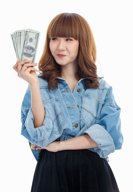 Mujer asiática de cabello castaño sosteniendo billetes estadounidenses que se extienden en su mano, ella piensa que cómo usarlo, foto de estudio sobre fondo blanco.